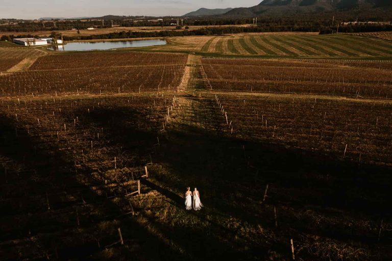 Two brides walking through Hunter Valley vineyards at sunset at their wedding